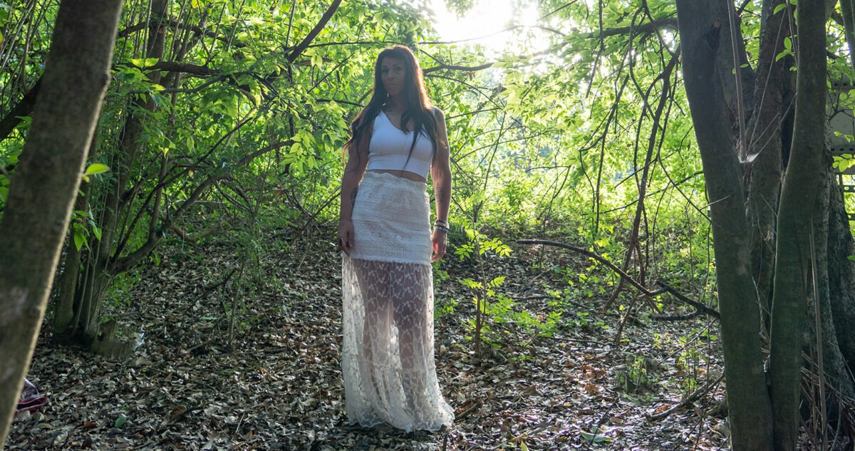 Lightworker Audrey Love stands in a forest, wearing white
