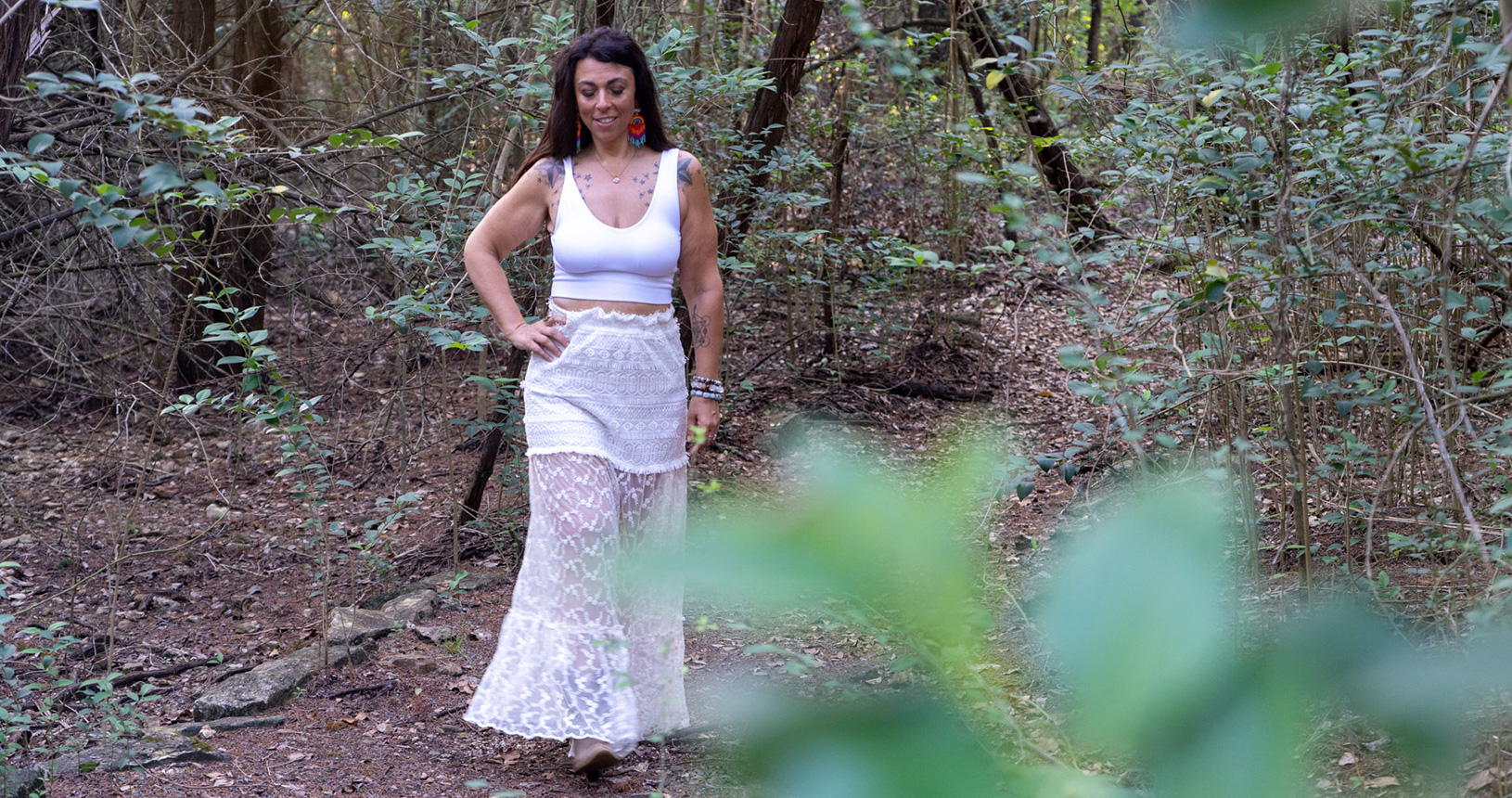 Lightworker Audrey Love stands in a forest, wearing white